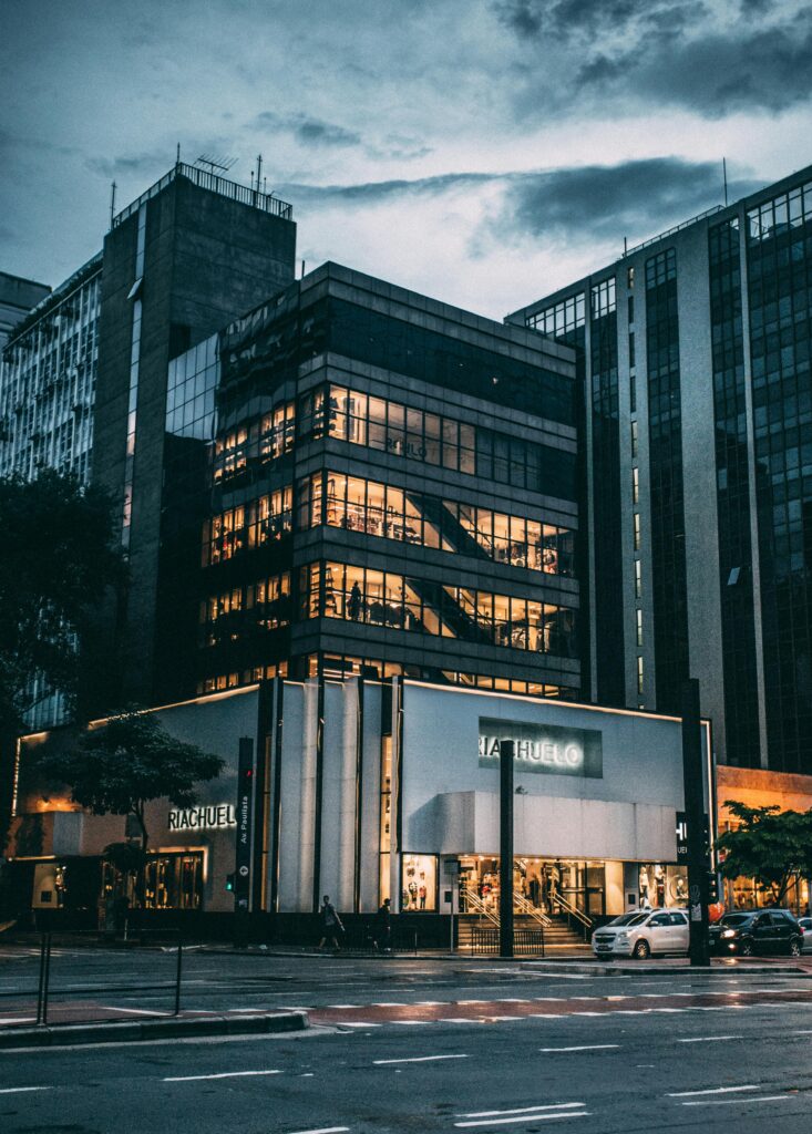 pexels-photo-65438-65438 Night view of a city block with illuminated store, modern architecture, and cloudy sky.